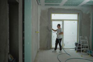 A man sprays paint on a wall while renovating an indoor room with professional equipment.